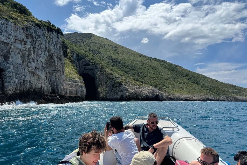 view of the entrance of Haxhi Ali Cave. In the photo are shown a group of people during a boat trip in front of the cave
